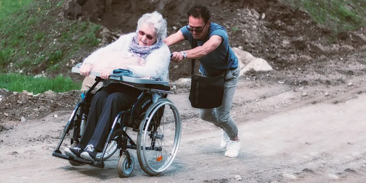 Un hombre tira de su madre por un camino embarrado