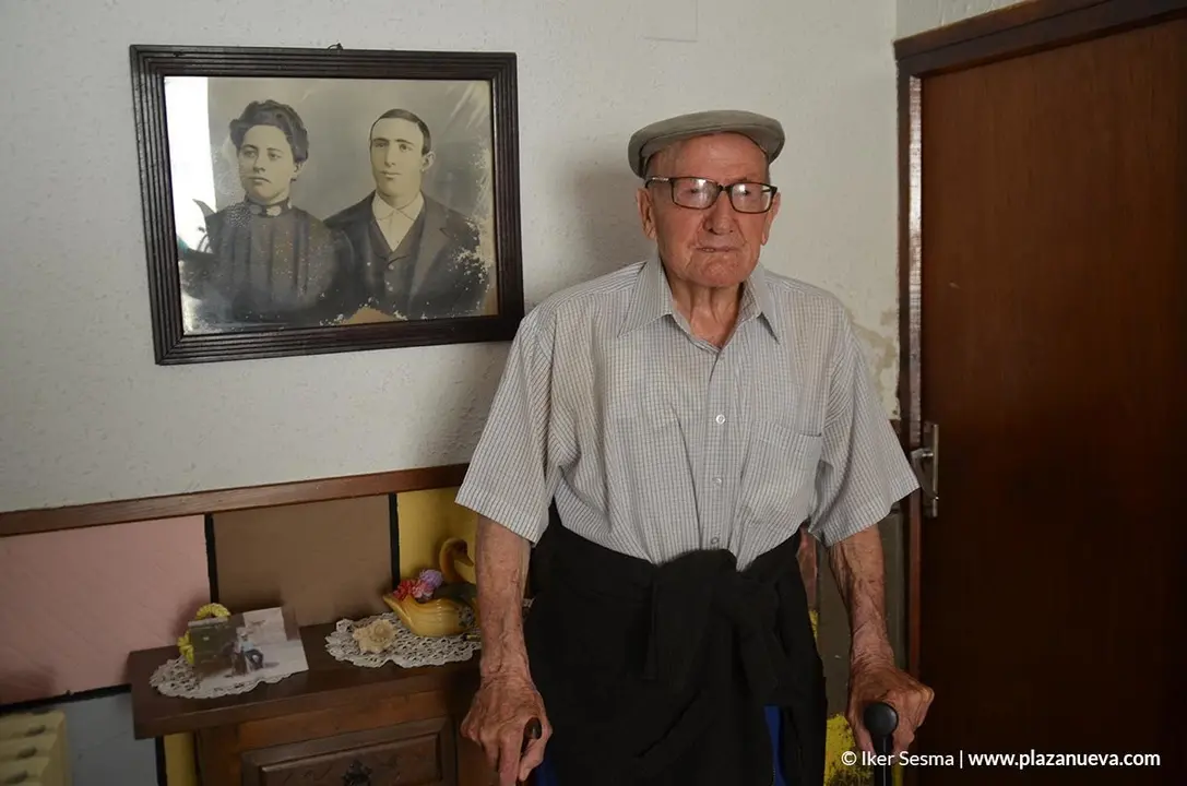 Hilario en la entrada de su casa, junto a un retrato de sus padres