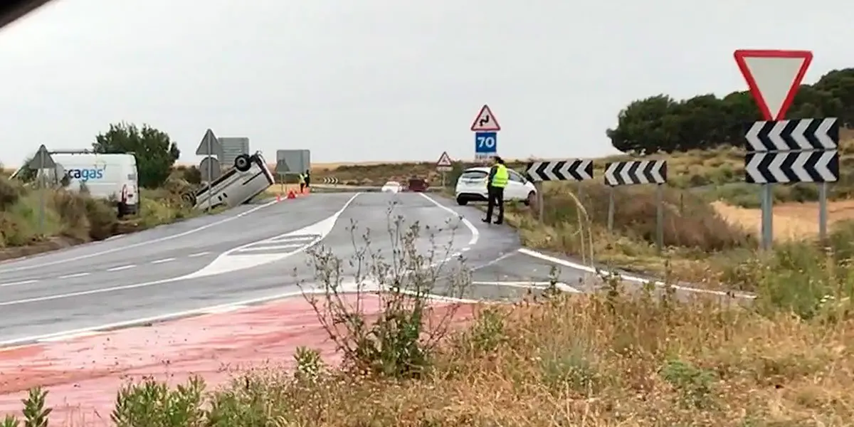 A la izquierda se observa a la furgoneta volcada en un lateral de la calzada