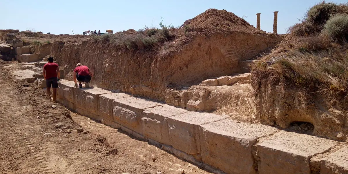 Dos estudiantes limpian los restos de lo que ser&iacute;a la muralla que cerraba la ciudad romana de Los Ba&ntilde;ales