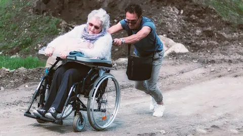 Un hombre tira de su madre por un camino embarrado