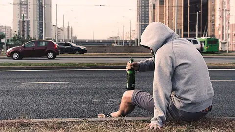Un joven bebe una cerveza en la carretera