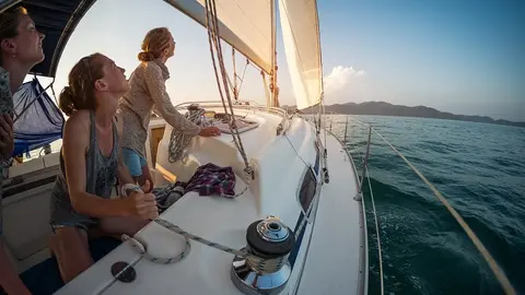 Three young women adjust the genoa sail after entering in a calm area of a tropical sea