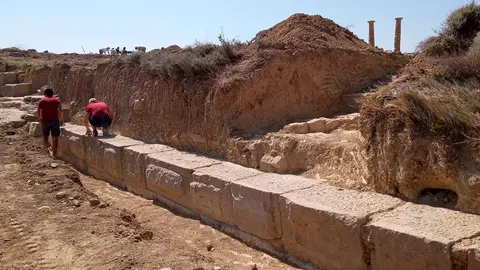 Dos estudiantes limpian los restos de lo que ser&iacute;a la muralla que cerraba la ciudad romana de Los Ba&ntilde;ales